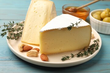 Tasty Camembert cheese with thyme and nuts on light blue wooden table, closeup