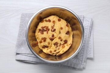 Dough with raisins in bowl on white wooden table, top view
