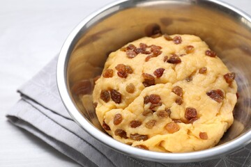 Dough with raisins in bowl on white table, closeup