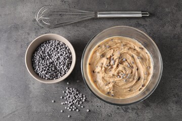 Raw dough with chocolate chips in bowl and whisk on grey table, flat lay