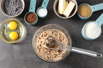 Raw dough with chocolate chips in bowl and ingredients on grey table, flat lay