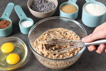 Woman making dough with chocolate chips at grey table, closeup