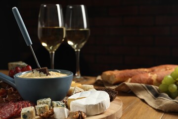 Fondue pot with tasty melted cheese, fork, different snacks and wine on wooden table