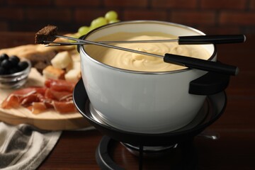 Fondue with tasty melted cheese, forks and piece of bread on wooden table
