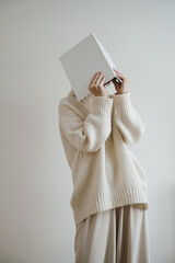 Woman in white wearing hiding face with book, album or notebook. Reading, studying concept. Neutral beige color. Blank cover sheet mock up with copy space - 785556013