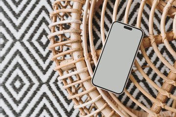 Mobile phone with blank screen on ornamental bamboo table and carpet. Flat lay, top view mock up with copy space. Bohemian, coastal, organic modern and tropical style