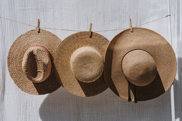 Three straw hats hanging over white cotton cloth with strong shadows. Sunbathing on a summer sunny day concept - 785556490