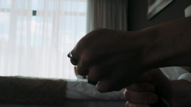 male hands open a bottle of champagne against the background of a bed and a girl