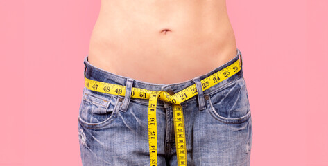 woman with a tape measure around her jeans showing waist measurement, dieting concept, close up.