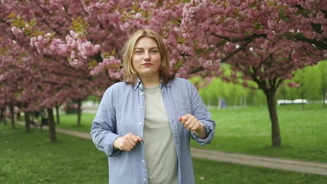 Portrait of happy young Caucasian woman listening music online in the city. Beautiful cherry blossom sakura in spring time over blue sky. Japanese sakura. High quality FullHD footage