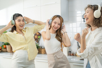Three joyful friends wearing headphones and dancing to music in a bright, modern kitchen.