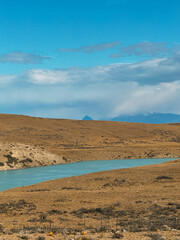 A dry, barren landscape with a river running through it. The sky is mostly clear, with a few clouds scattered throughout