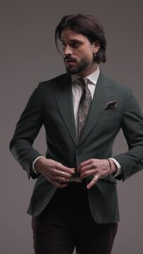 vertical video of sexy cool businessman in elegant suit walking, looking down, adjusting hair, holding hands in pockets and being cool on grey background