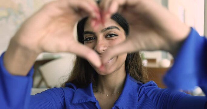 Serious beautiful young Indian woman getting positive, happy, showing finger heart, looking at camera through finger frame, smiling for portrait, expressing, love, gratitude