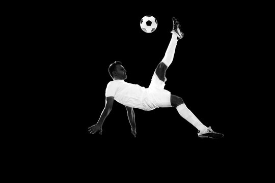 Dynamic image of motivated male soccer playing in motion, training, hitting ball and falling down on lack background. Monochrome. Concept of professional sport, game, competition, tournament, action