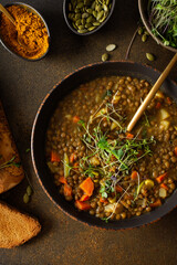 Healthy vegetarian lunches, brown lentil soup with tomatoes and carrots, potatoes and curry spices, toasted croutons, bowl with soup on cutting board on brown background