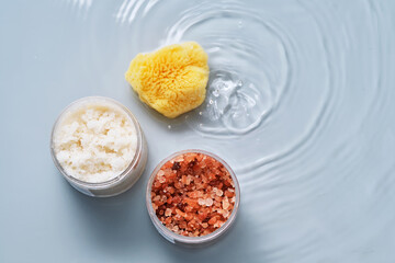 Body scrub, bath salt and natural sponge on a blue background with water.