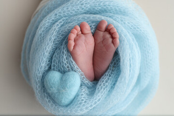 The tiny foot of a newborn baby. Soft feet of a new born in a blue wool blanket. Close up of toes, heels and feet of a newborn. Knitted blue heart in the legs of a baby. Macro photography. 