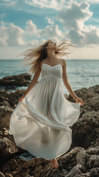 Modella con abito bianco su una scogliera che allarga le braccia mentre la brezza le muove i capelli.