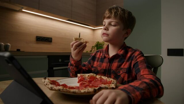 kid relishes a tasty pizza slice while engrossed in a tablet computer. Perfect for portraying the modern blend of tech and mealtime enjoyment