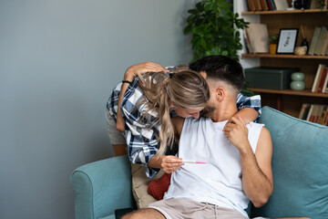 Young happy couple, pregnant woman showing positive pregnancy test to the man at their apartment....