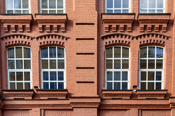 Fragment of facade of old classic red brick building with four large windows with white frames