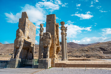 Imposing Lamassu statues stand tall, casting intricate shadows amidst the ancient ruins of Persepolis, Iran. Captured on a bright day with the blue sky and clouds. - Powered by Adobe