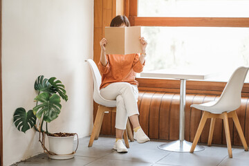 Close up teenage girl holding and covering book or magazine in reading room at home or cafe, copy space concept.	