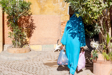 muslim woman with bags in hands in traditional long attire walks down street Red City Marrakech,...