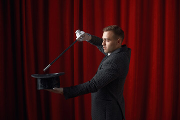 Young handsome illusionist performing magical trick with wand and hat