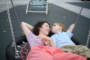 Obraz premium Happy Young mother playing with her son on the playground, hugging, laughing. having fun together on the weekend sunny day. School playground. High quality photo