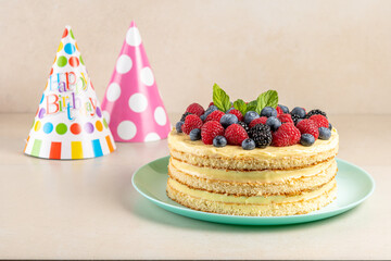 Homemade cake with fresh berries and birthday hat on bright background.