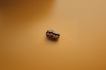 A single brown coffee bean on a minimalist cream colored surface