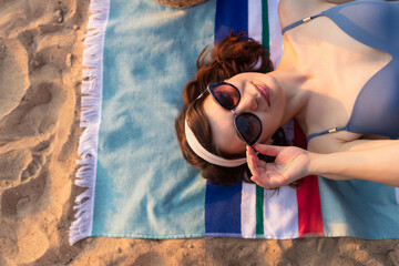 Young woman in sunglasses and blue swimsuit lying on the beach striped towel. Summer vacation fashion and beauty lifestyle concept