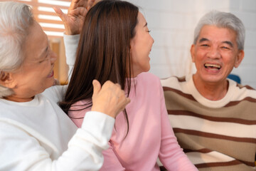 Obraz premium Asian Family Bonds: Daughter's Laughter Echoes in the Home as Grandfather and Grandmother Enjoy Retirement, Sharing Hugs and Smiles on the Sofa, A Precious Elderly Bonding Moment