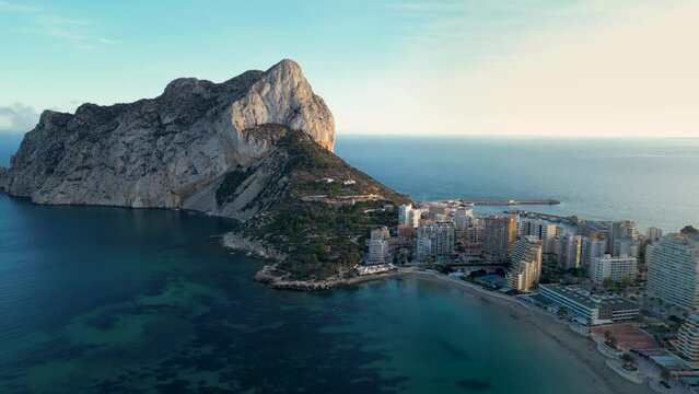 Part of Calp city and Ifac Mountain, perspective from above. Beautiful sunset reflecting on mountain and buildings. Famous travel destination in Alicante Province, Spain. Drone forward.