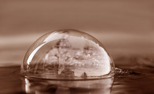 In einer Seifenblase in Peach Fuzz auf einer Wasseroberfläche spiegelt sich die Landschaft