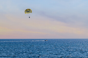 Flying parasailing parachute tied to a motorboat in the sea. Beautiful seascape in the evening with tourist entertainment