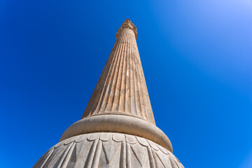 A towering column adorned with intricate carvings stands against the clear blue sky at Persepolis....