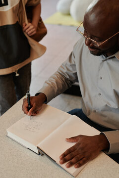 High angle of young modern author signing his book for one of fans during meeting with public in library