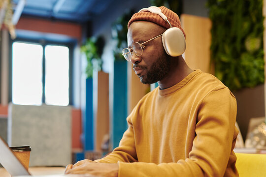 African American guy in headphones looking at laptop screen while watching educational online video in library