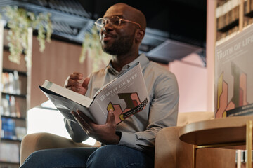 Open book in hand of young African American author sitting in front of camera and making presentation speech at event