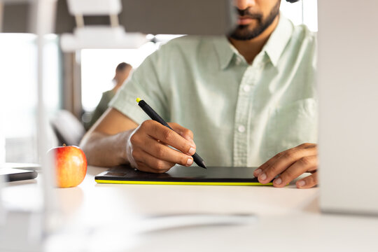Asian male professional drawing on digital tablet in a modern business office, wearing a green shirt