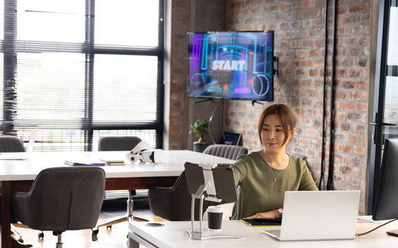 Asian middle-aged woman with light brown hair working at laptop in a modern business office