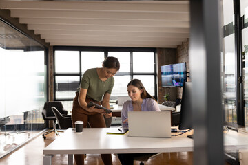 Asian mature professional showing tablet to young Caucasian colleague in a modern business office