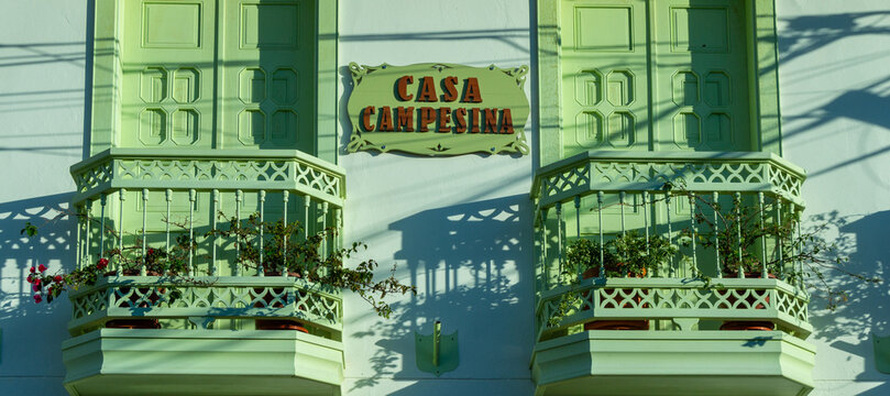 Jerico, Antioquia, Colombia, August 8 2023 : Beautiful traditional facade in the historical village, pueblo, of Jerico, Jeric&oacute; . Colored wooden sculptured windows and balconies. Vegetation.