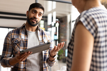 Asian male colleague holding tablet, talking to Caucasian female colleague