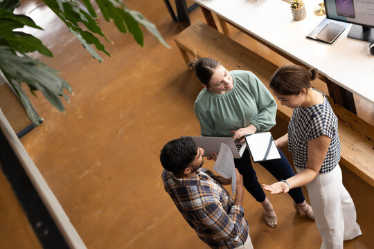 Middle-aged Asian female professional showing tablet to young colleagues in a modern business office