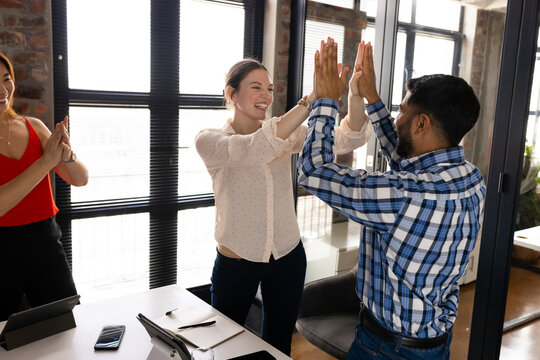 A diverse team is celebrating in a modern business office, high-fiving and clapping