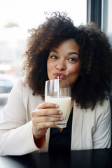 woman with curly hair is drinking milk from a glass. She is smiling and she is enjoying her drink